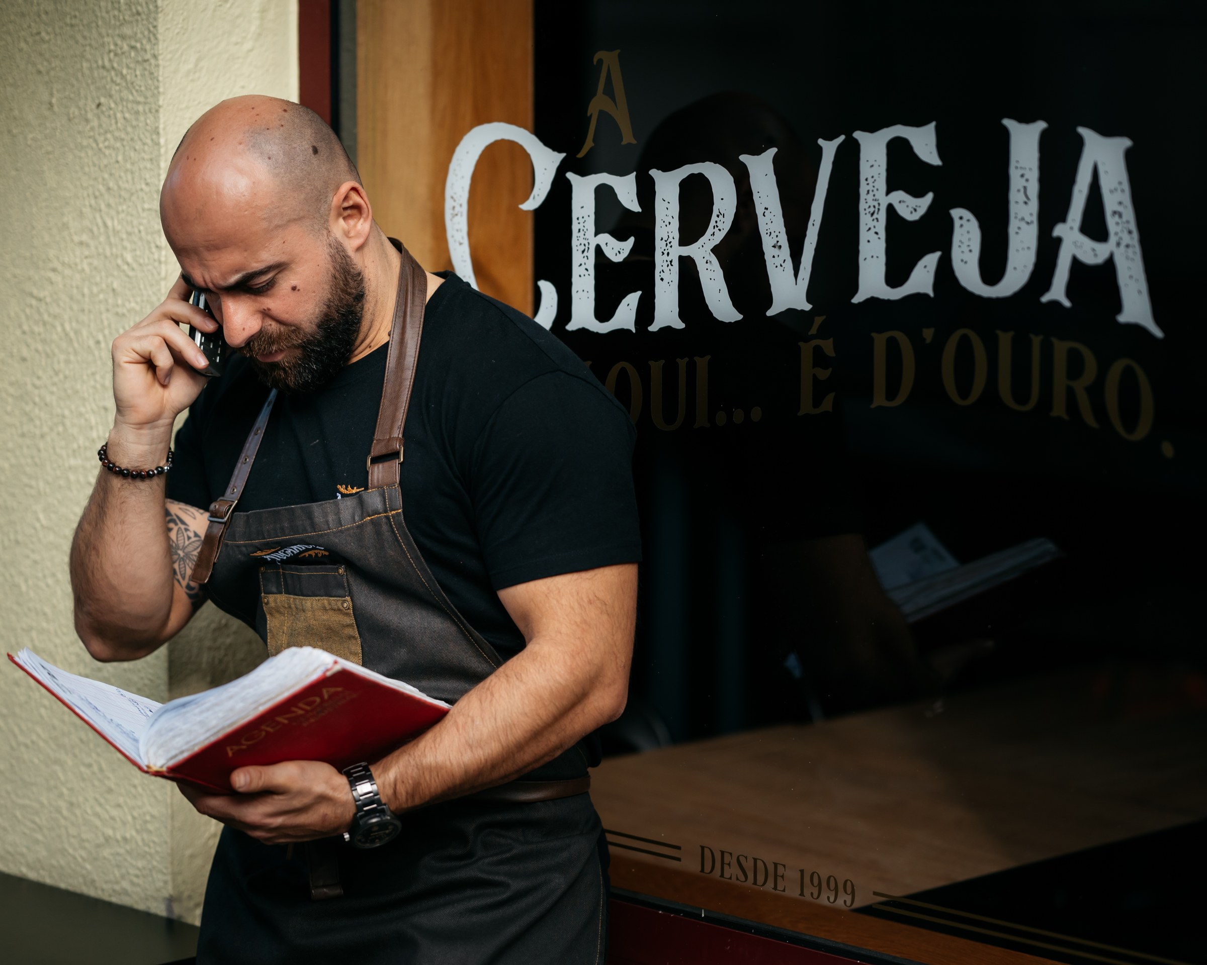 Um dos sócios ao telefone, com um caderno na mão, junto à montra do restaurante
